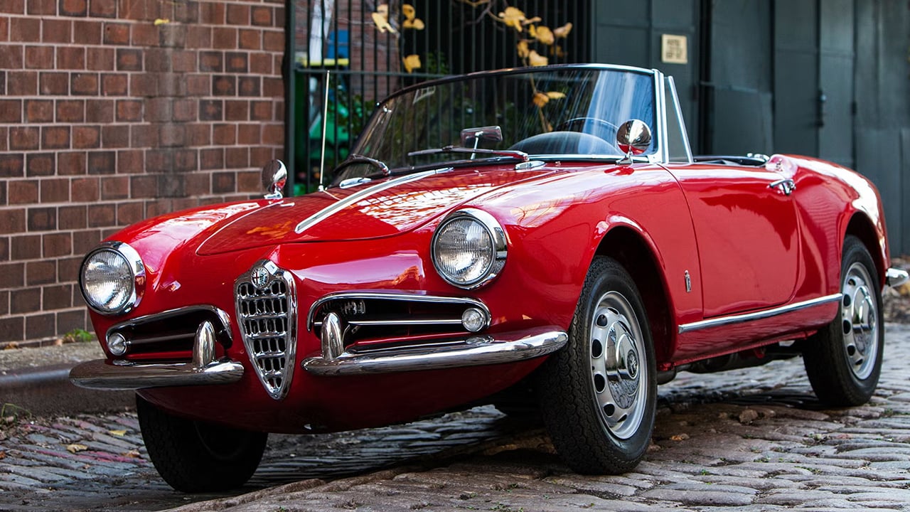 Vue 3/4 avant et latérale de l'Alfa Romeo Spider 1967 garé en bord de rue pavé