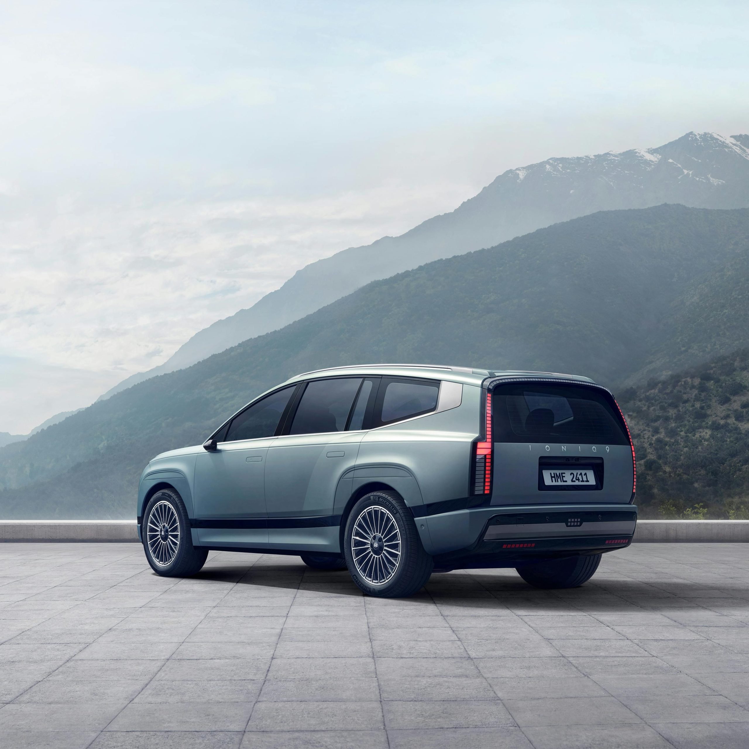 The image depicts a Hyundai IONIQ 9 parked against a mountain backdrop