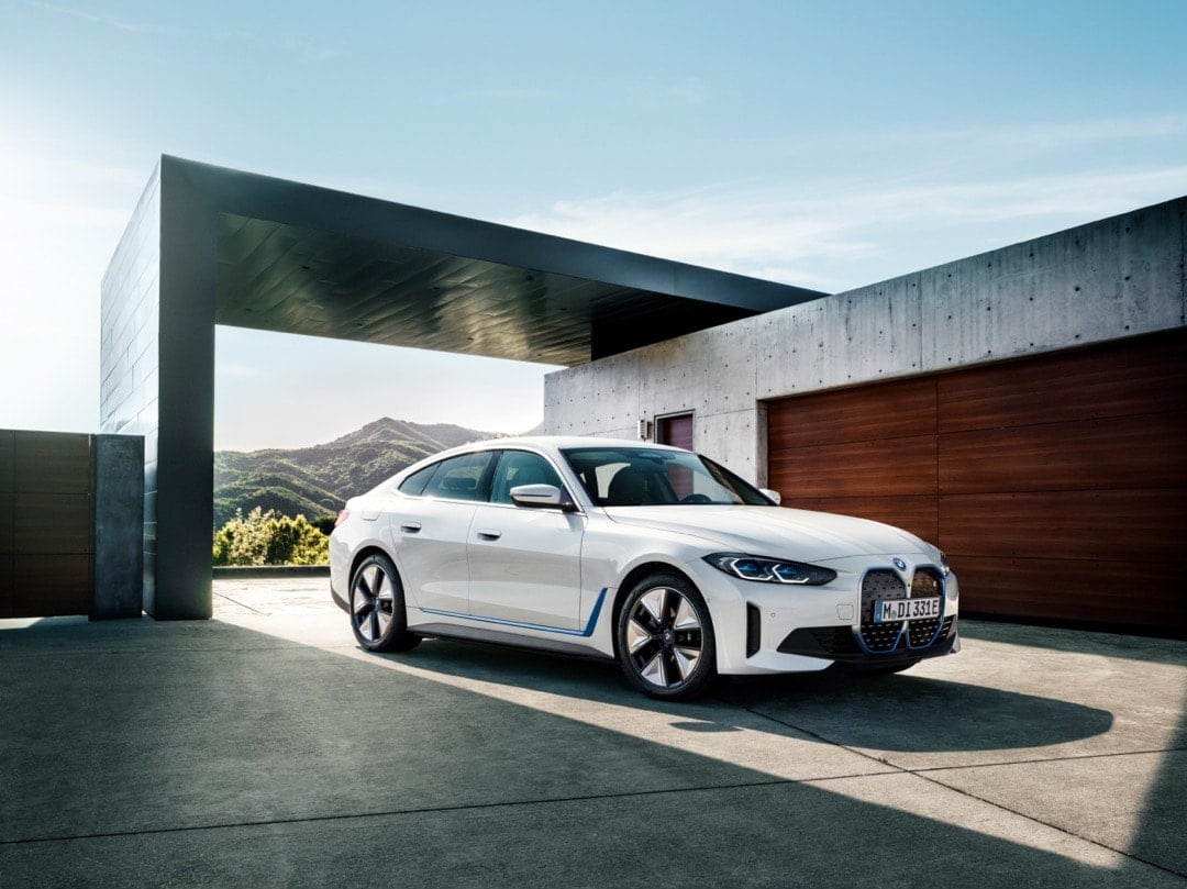 Front 3/4 view of the 2023 BMW i4 parked in the driveway of a house.