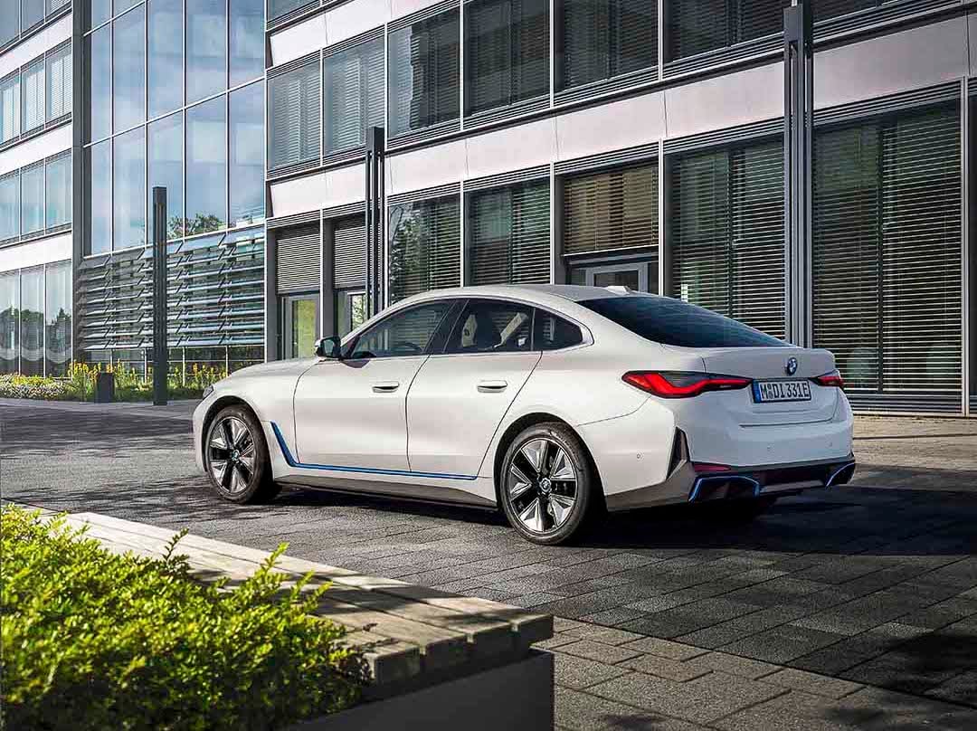 Vue 3/4 latérale-arrière de la BMW i4 eDrive40 2022 blanche garée au bord d'un édifice