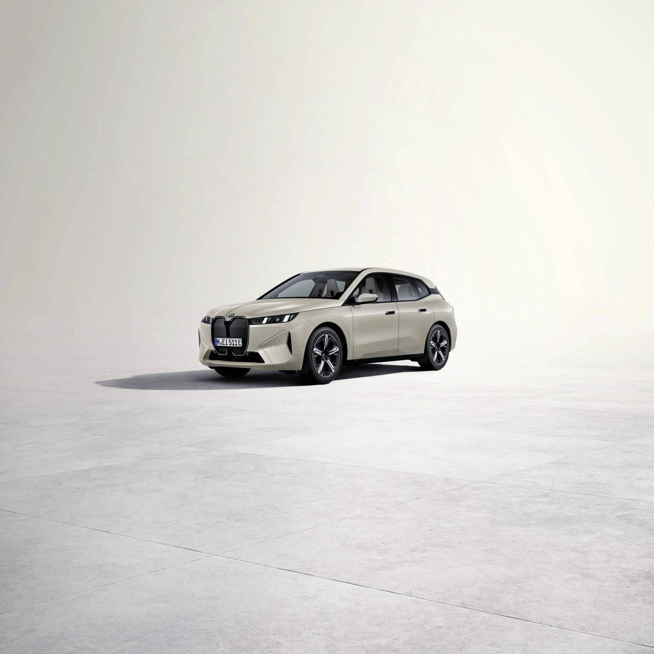 2026 BMW iX xDrive45 sand beige three-quarter front view on a minimalistic light background with monolithic design and prominent BMW grille.