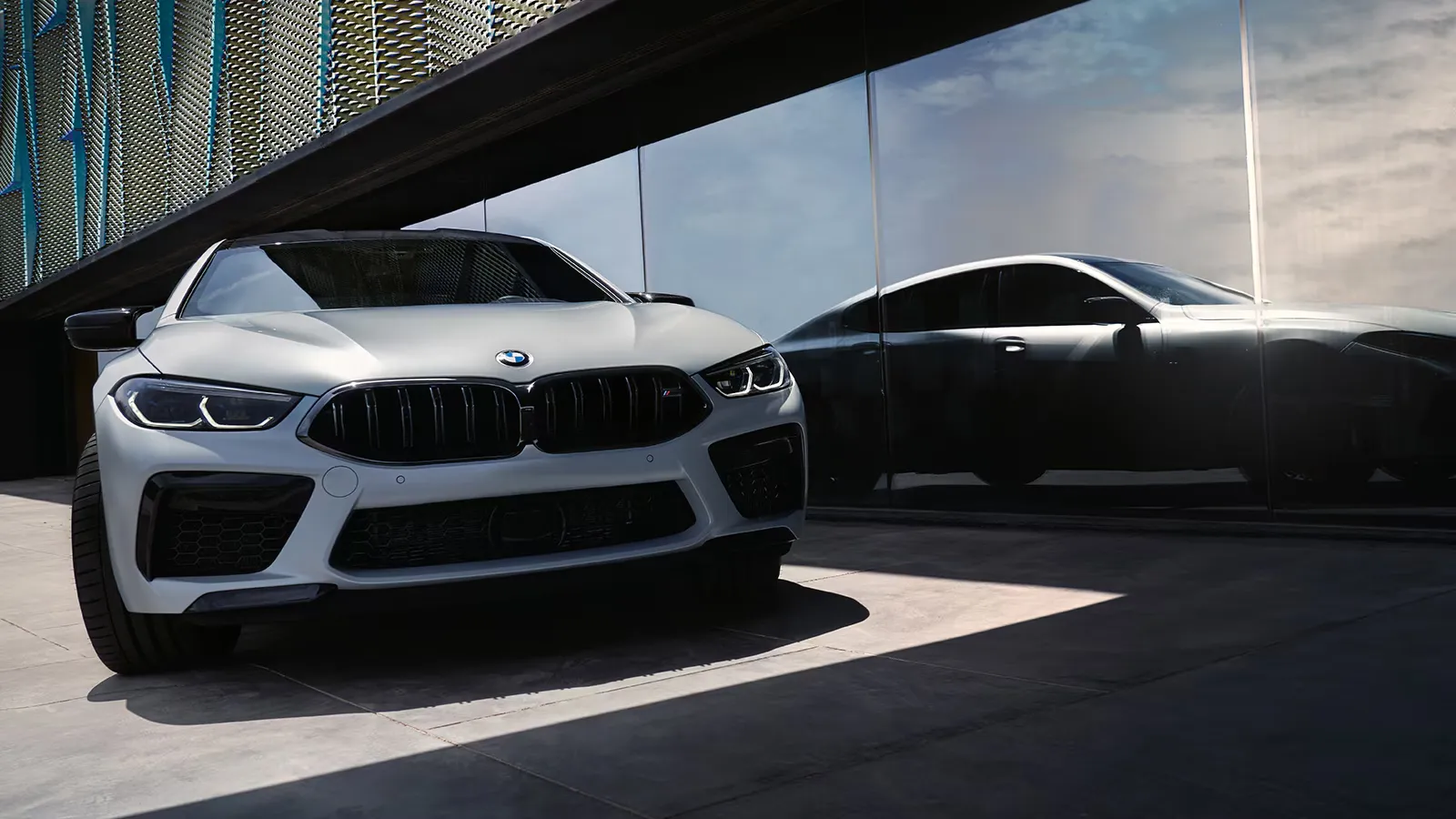 White 2025 BMW M8 Gran Coupé three-quarter front view in a modern urban setting.