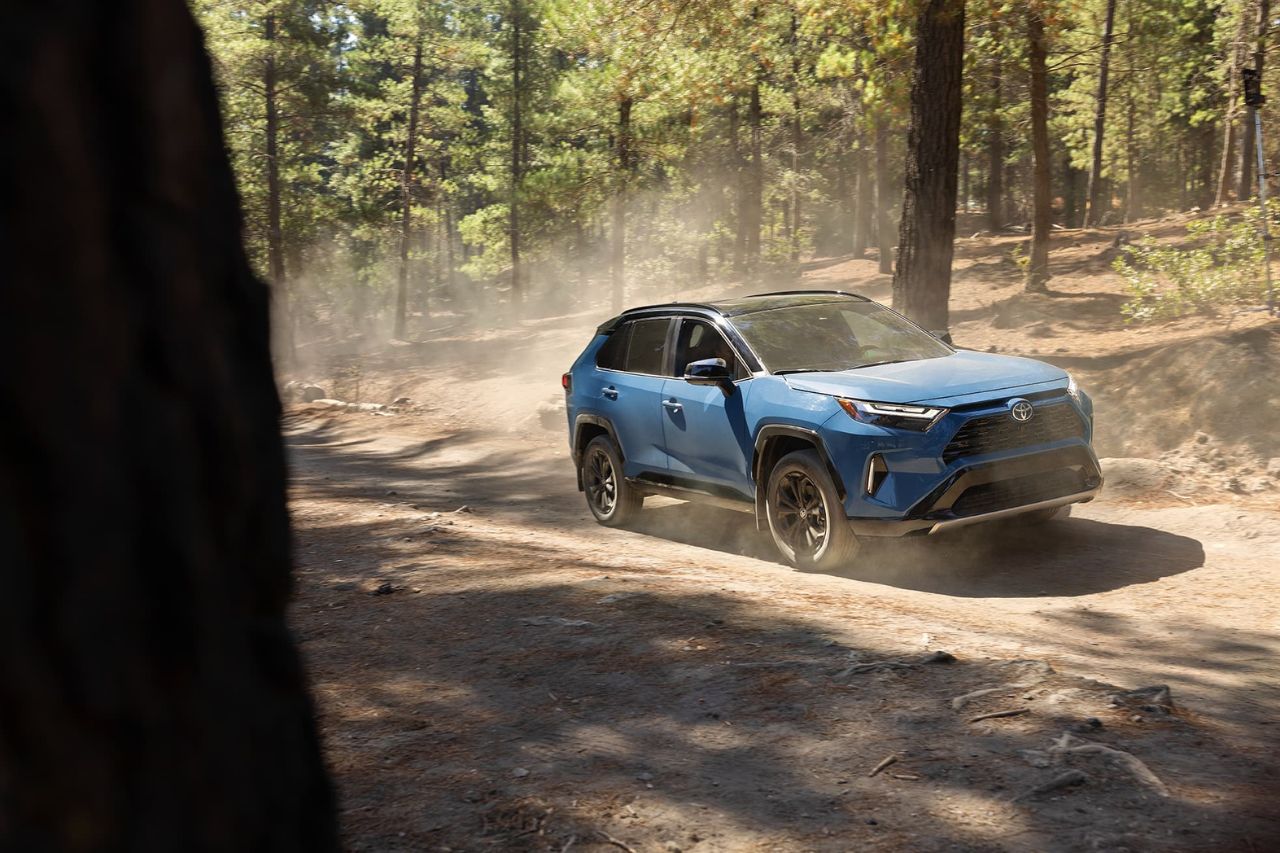 A Toyota RAV4 vehicle driving down a dirt road in a forest.