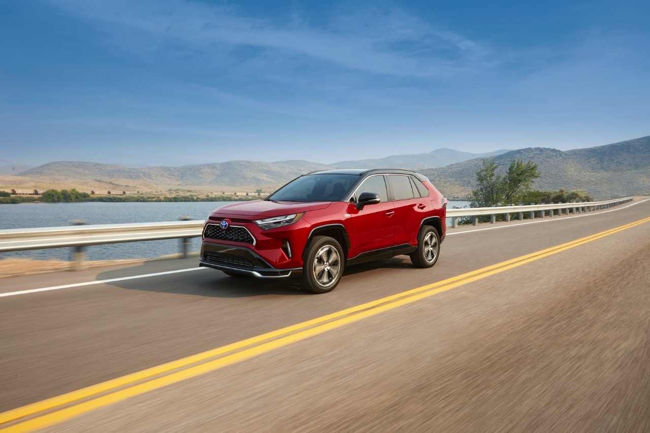 A red 2024 Toyota RAV4 drives down a sunny highway.