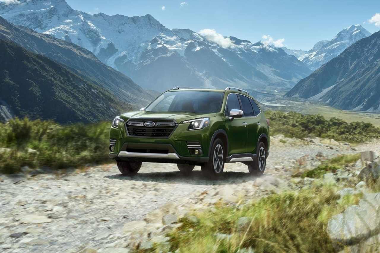 A green Subaru Forester SUV is parked on a trail in a mountain valley.