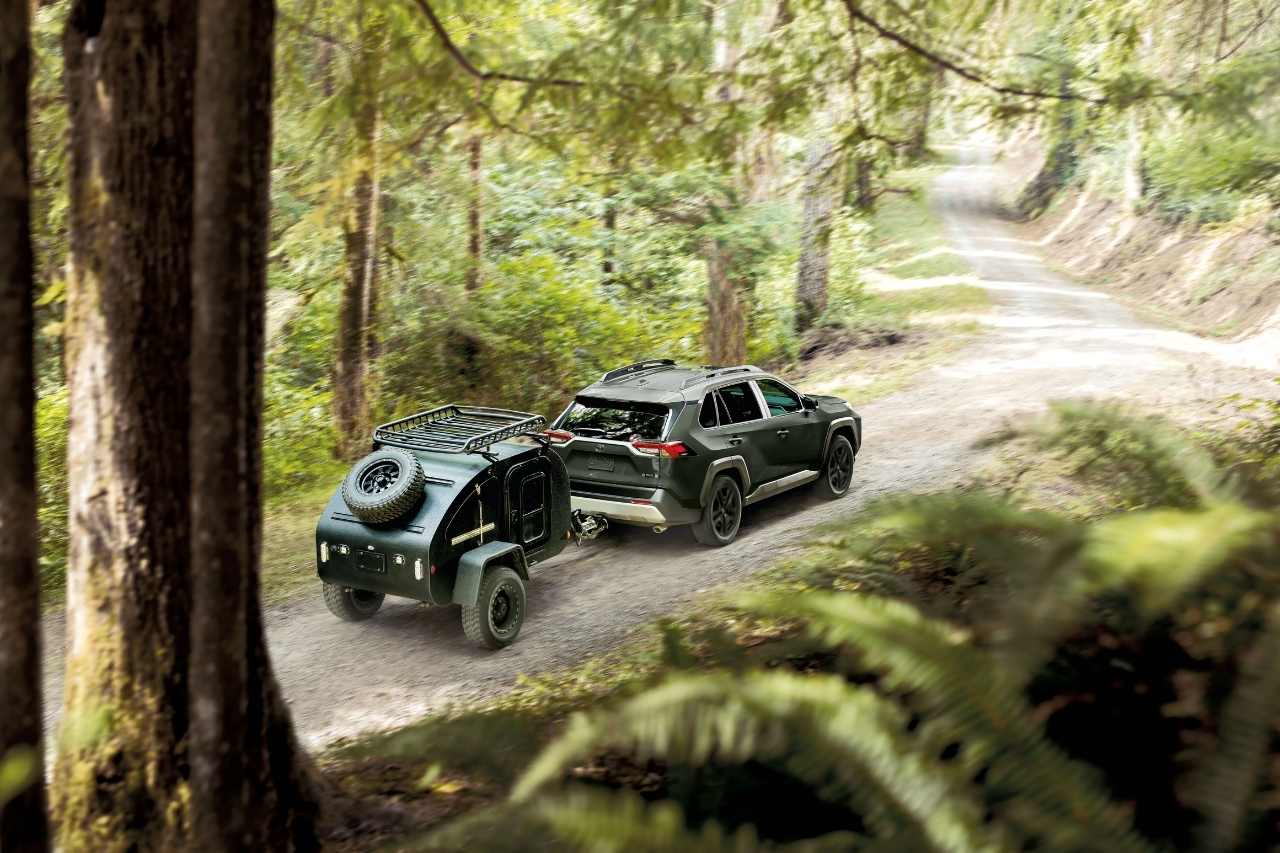 A green RAV4 sports utility vehicle carries a camper and drives down a dusty forest road.