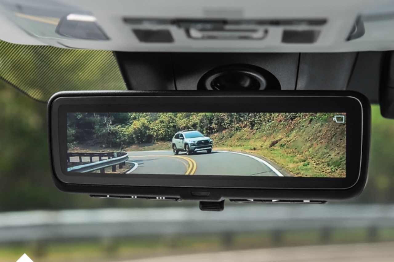 A digital display rearview mirror in a Toyota vehicle, showing a vehicle driving behind them on a mountain road.