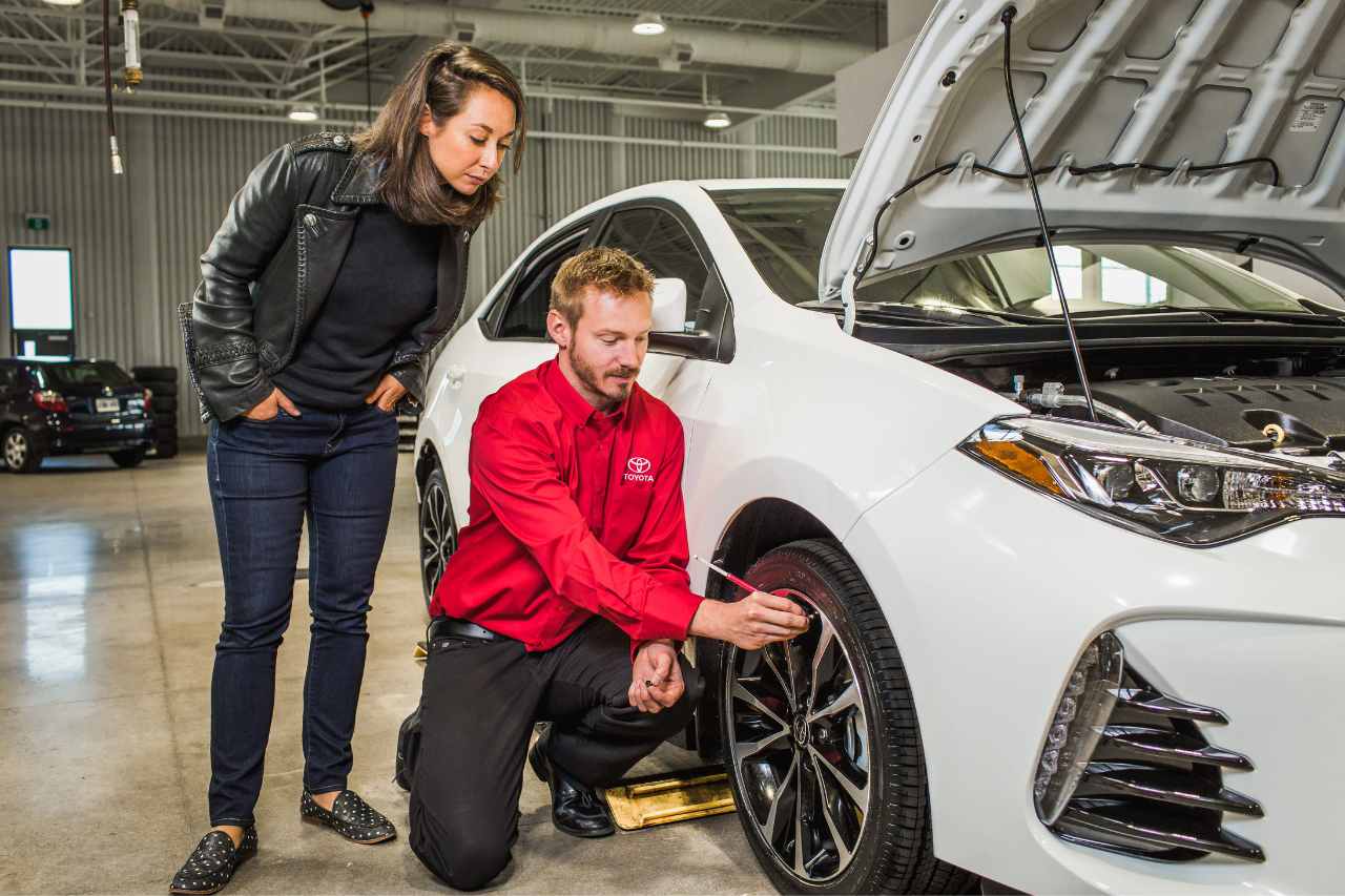 A Toyota Service technician checks the vehicle's tires in front of a customer.