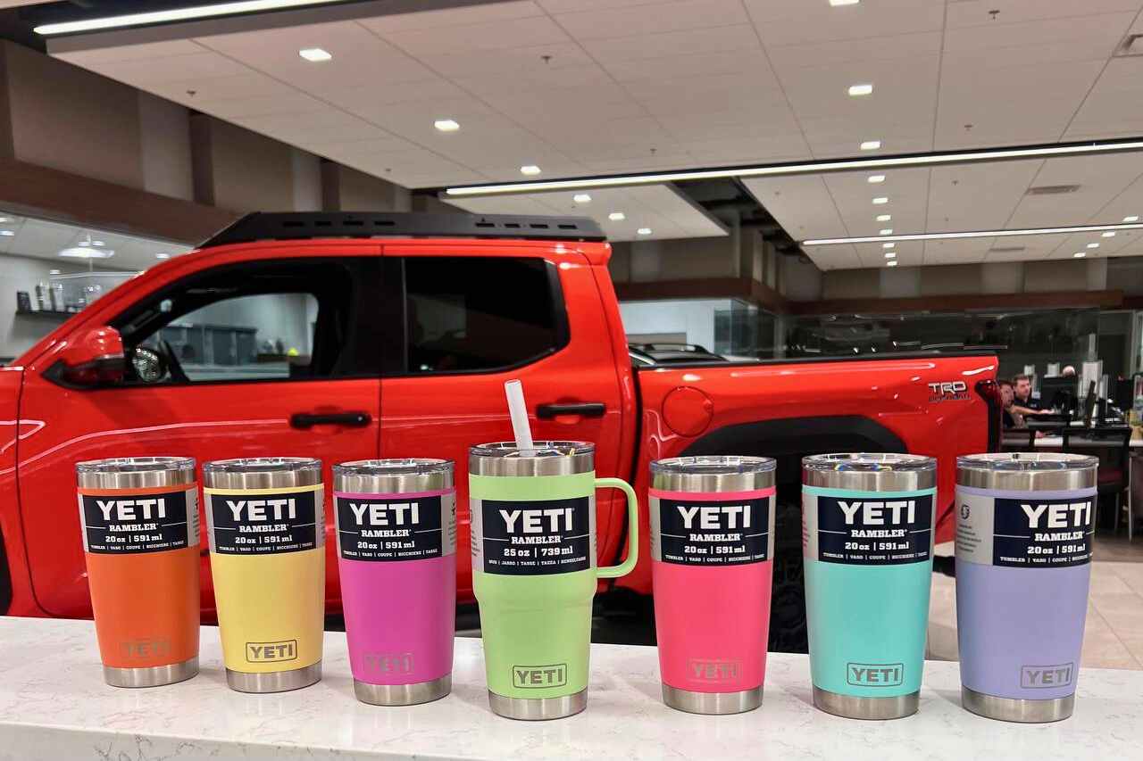 A row of seven YETI drinkware in various colours are posed in front of a red Toyota Truck.