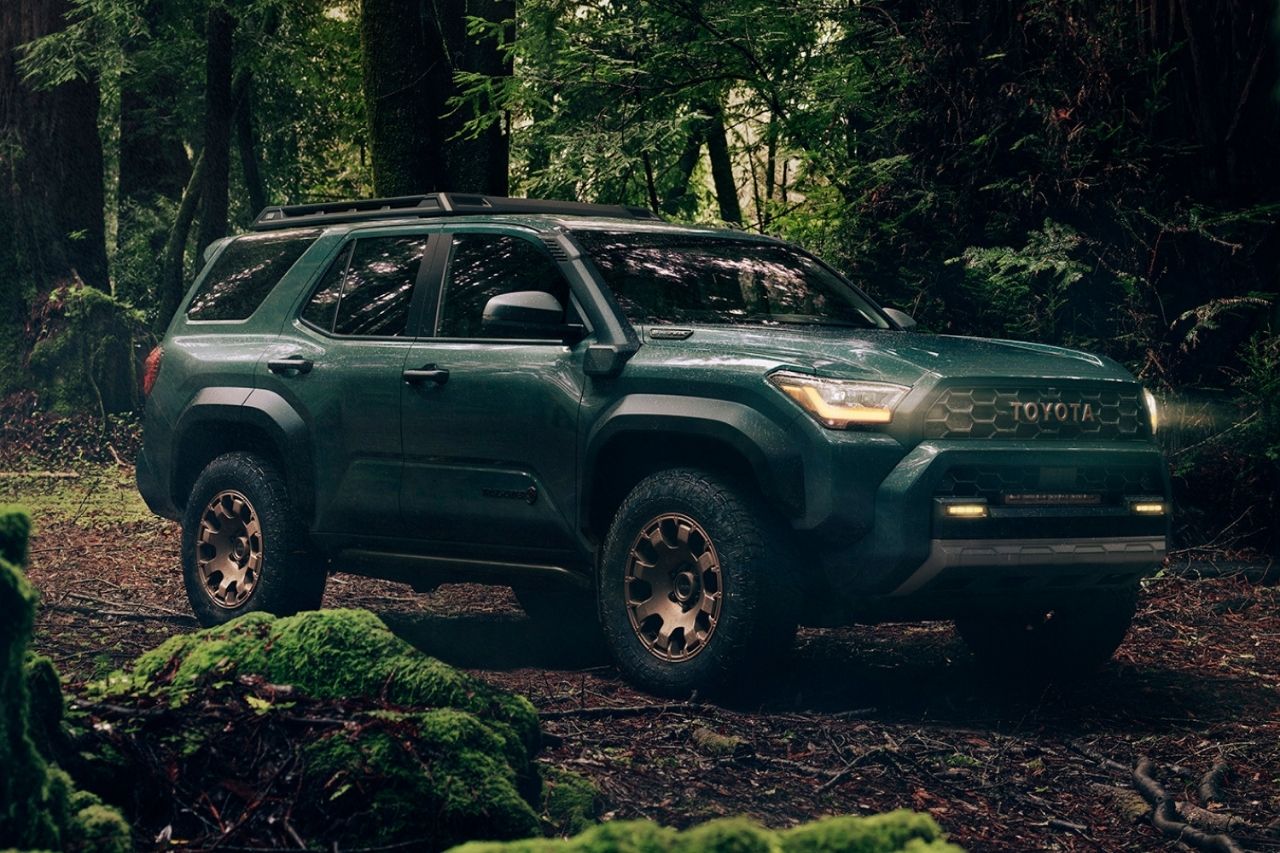 The Toyota 4Runner SUV in a green colour is off-roading in a moody forest.