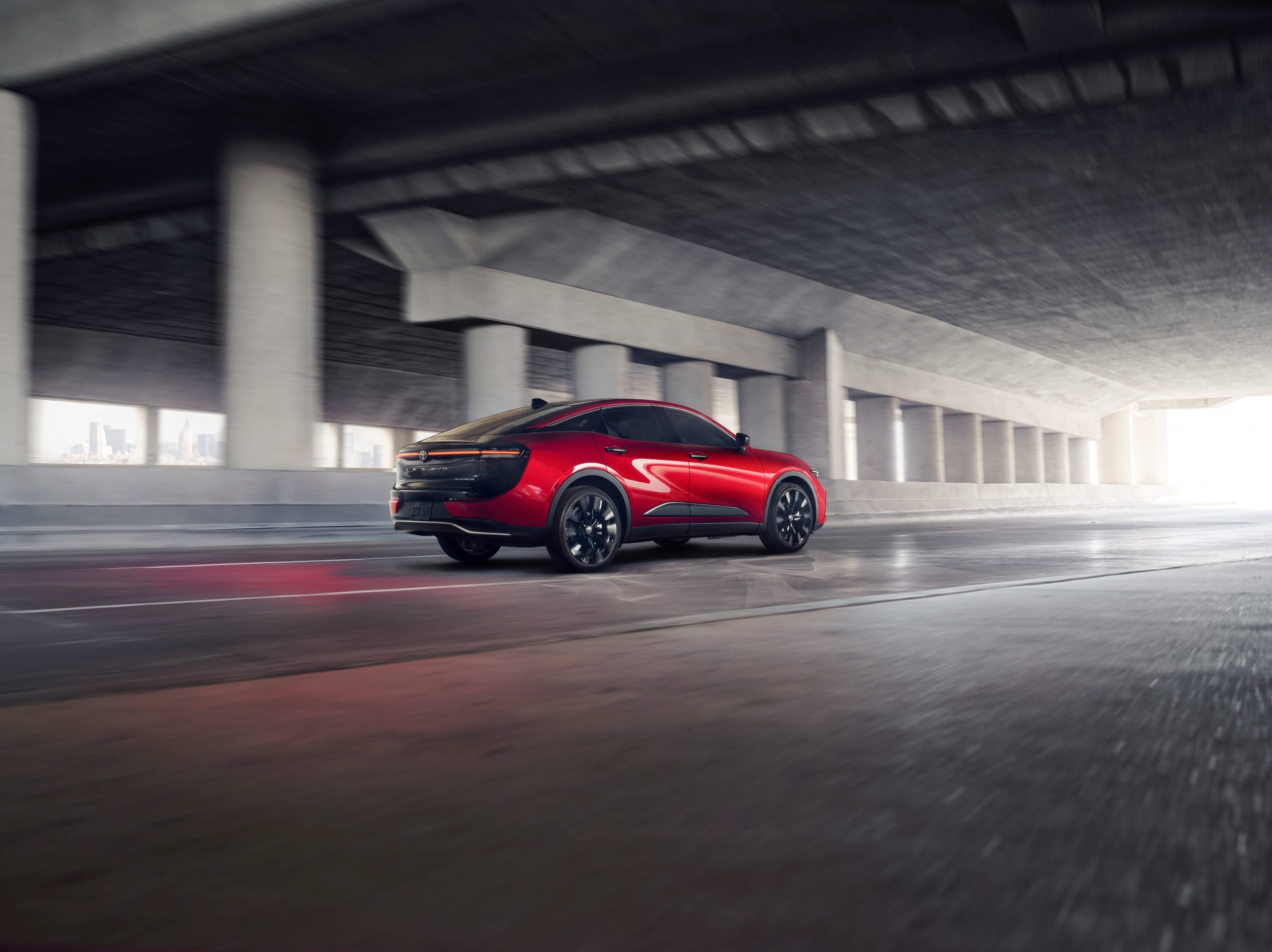 A brand-new hybrid Toyota Crown in a bright red colour drives down a highway tunnel.