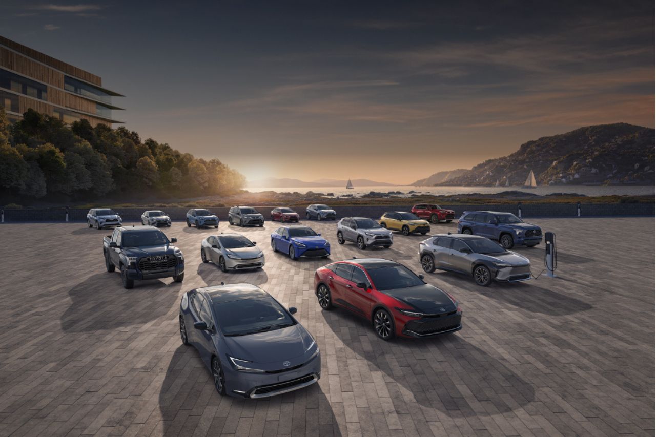 A group of electric vehicles are parked on a cement pad in front of a sunset.