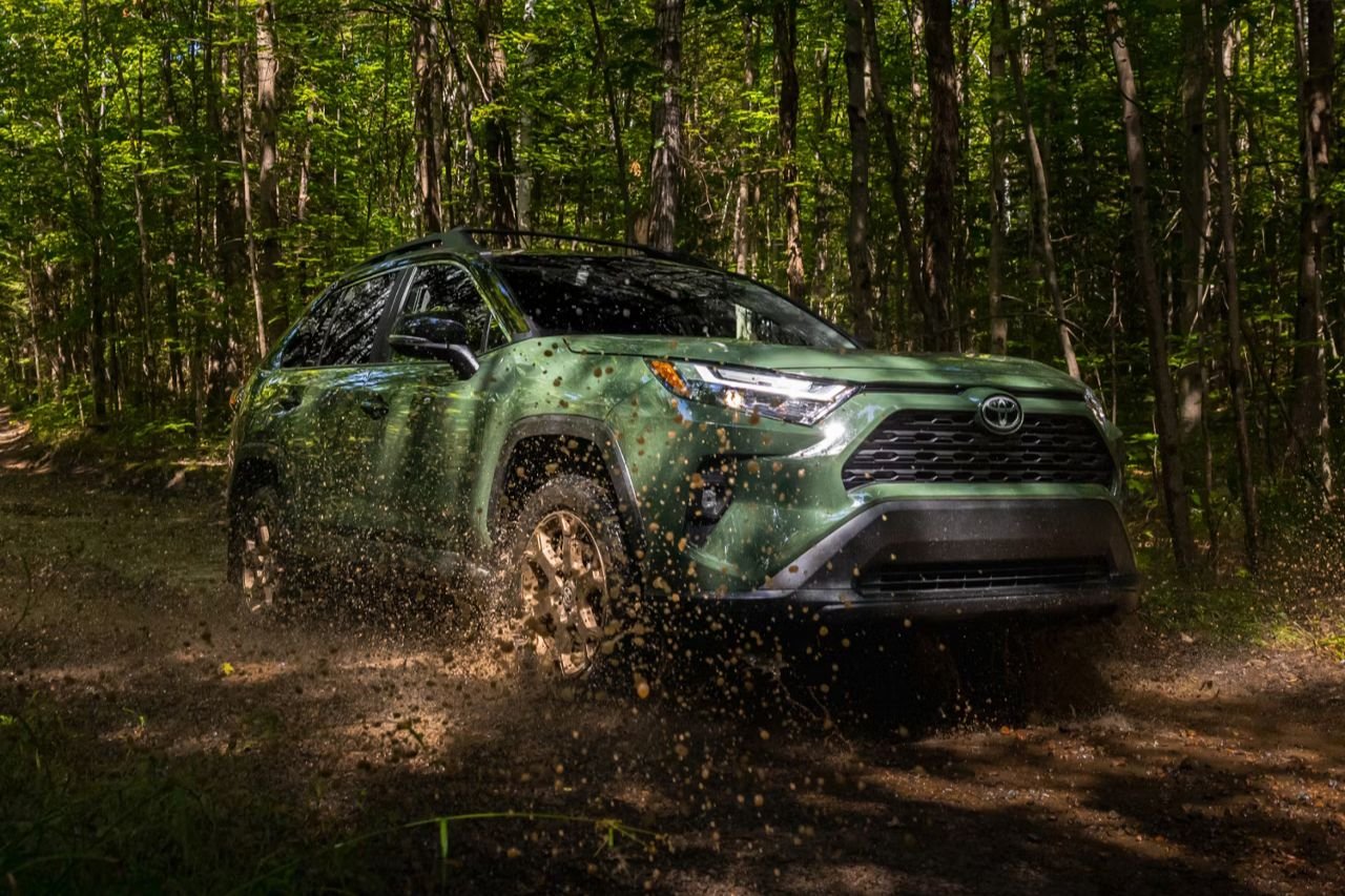A green Toyota RAV4 drives down a muddy, dirt road in the middle of the forest.