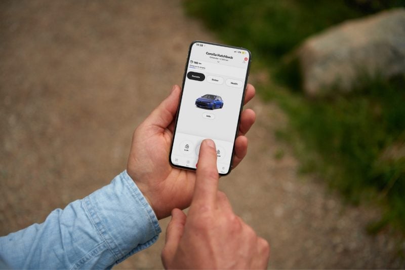 A man in a blue shirt holds his smartphone and explores the Toyota Remote Connect app that's connected to his Toyota Corolla.